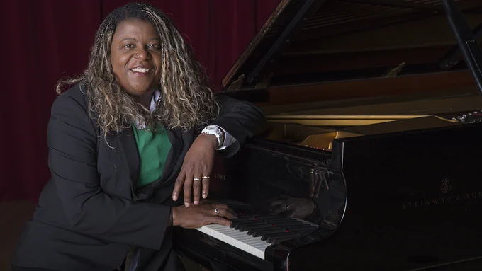 Dee Spencer smiles while seated at a grand piano