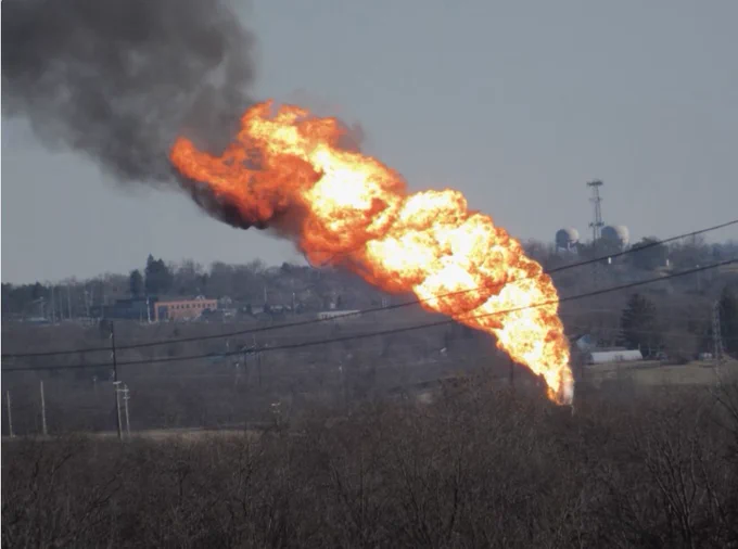 More zoomed out photo of huge flare with black smoke from the shell plant you can see water towers and buildings in the background
