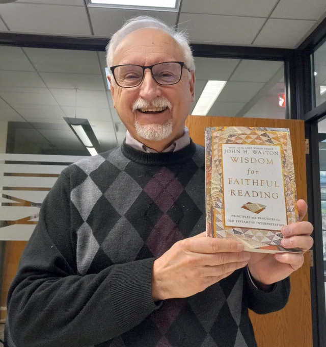 Dr. John Walton holding a copy of Wisdom for Faithful Reading