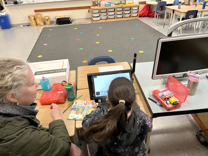 An educator sitting with a student in front of a Cloverbook magnifier.