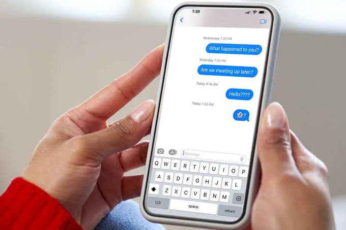 A pair of hands holding a cell phone and the phone screen is displaying a stream of unanswered text messages. 