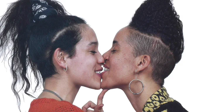 Julie Tolentino and Lola Flash touch bottom lips in an almost-kiss. This panel is one-third of the full Gran Fury advertisement, "KISSING DOESN'T KILL: GREED AND INDIFFERENCE DO," 1989.