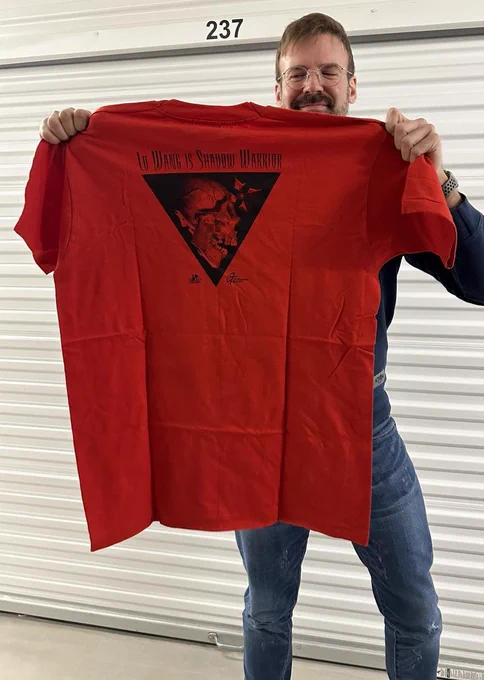 Apogee's Executive Producer, Jeron Moore, is holding a vintage blood-red t-shirt featuring "LO WANG IS SHADOW WARRIOR" text above an upside triangle with a shattering skull.
