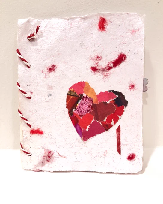 Handmade Valentine’s card made from recycled, handmade paper with yarn inclusions, and a scrap paper heart near the bottom. Stitched with red-and-white paper twine.