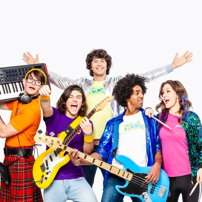 Andy Day stands behind 4 musicians in a colourful array of clothing.