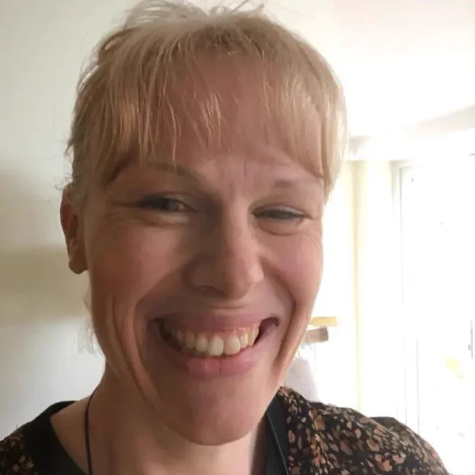 A selfie of Sam who is sporting a brilliant smile, showing her teeth. She has blonde hair, and is wearing a speckled brown top, with the thread of a necklace just visible on her neck.