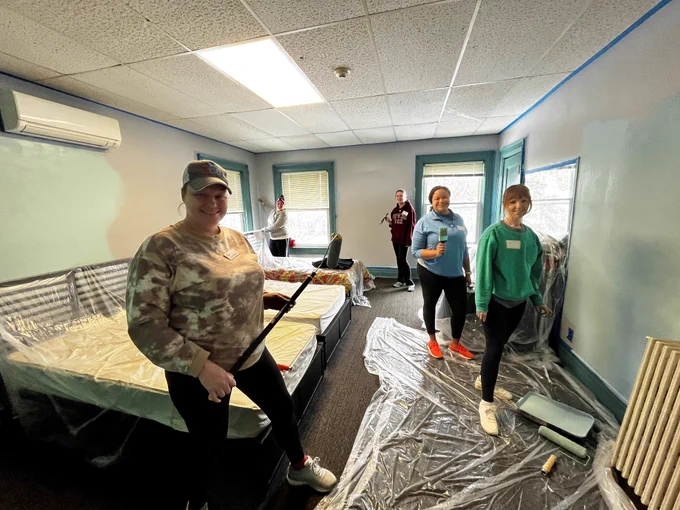 Members painting a bright room a light mint green color.