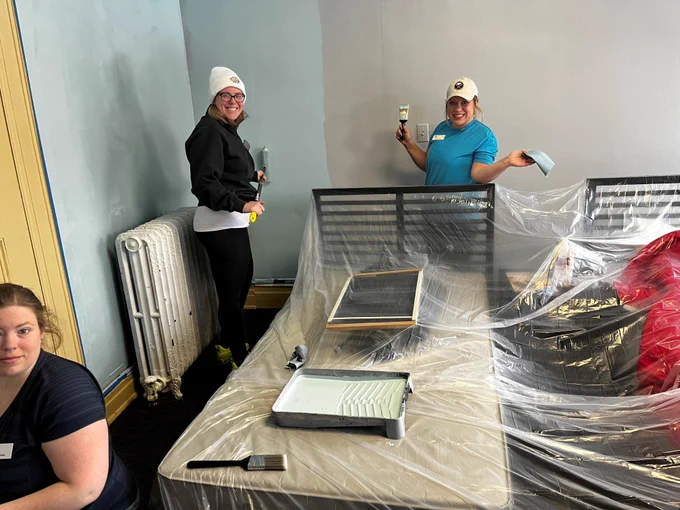 several JLB members painting a room. Furniture in the middle of the room is covered in plastic.