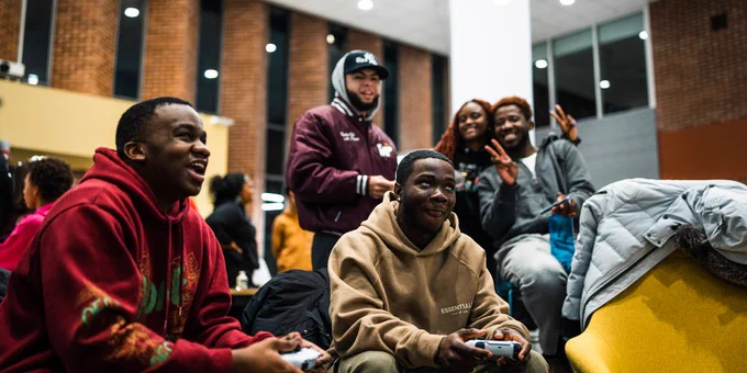 Five students sitting together, focused on playing a video game.