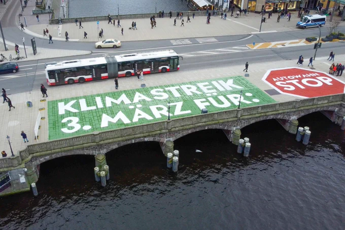 auf einem großen Schriftzug auf einer Brücke wird der nächste Klimastreik und das Thema angekündigt. In einem grünen Feld steht 'Klimastreik 3. März für' und in einem Stoppschild daneben steht 'Autowahn STOP'