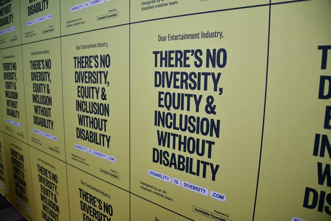 Close up on a yellow step-and-repeat displaying the words "There's no diversity, equity & inclusion without disability"
