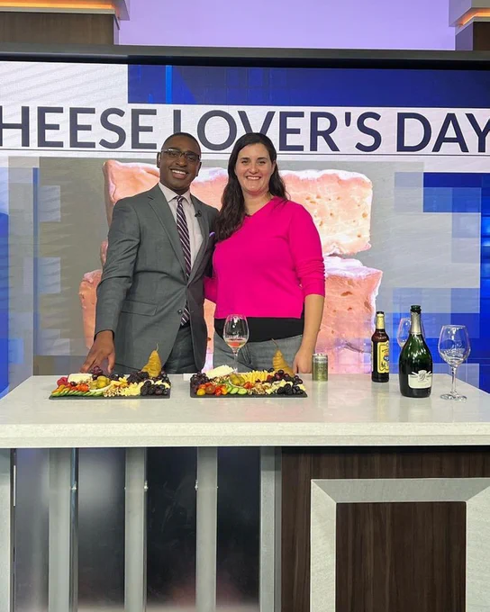 Cheesemonger Alice Bergen Philips and DC News Now Anchor Cory James smile in the studio, the cheese boards on a table in front of them.