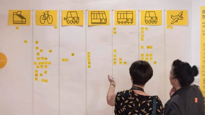 Two people look onto a board of travel options as part of Super Vernaculars, Exhibition View, BIO27, 2022.