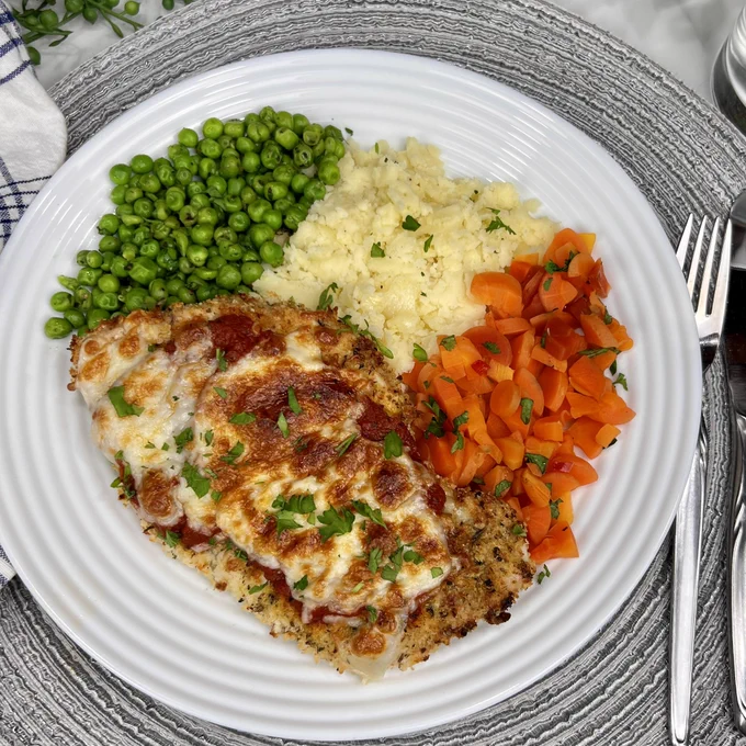 Baked chicken parmigiana on plate with veggies and mashed potatoes