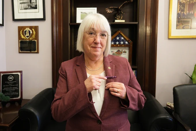 A photo of Senator Murray smiling and pointing to a crayon lapel pin on her suit jacket.