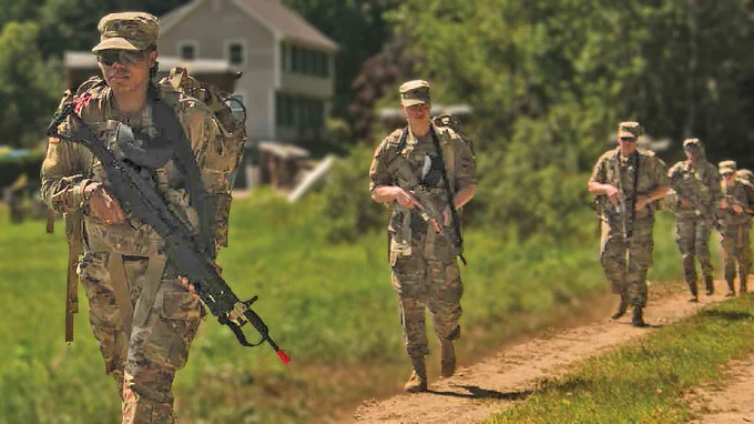 Five Soldiers wearing backpacks and holding guns walk on a dirt track. There is a house and woods in the background. (Photo Credit: Staff Sgt. Ray Boyington, 362nd Mobile Public Affairs Detachment; modified by the Army Geospatial Center)