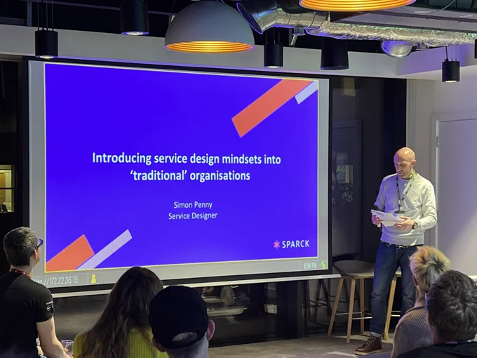Simon stood by his first slide. Slide reads 'Introducing service design mindsets into traditional organisations'