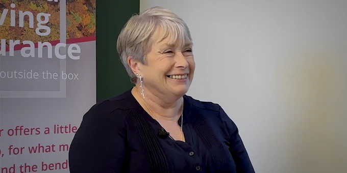 Smiling lady with short silver hair, blue shirt and silver earrings