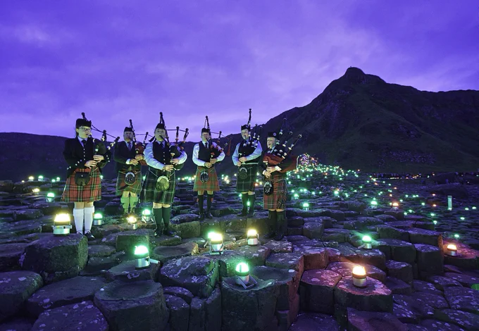 A group of people playing the bagpipes next to a mountain, surrounded by Geolights.