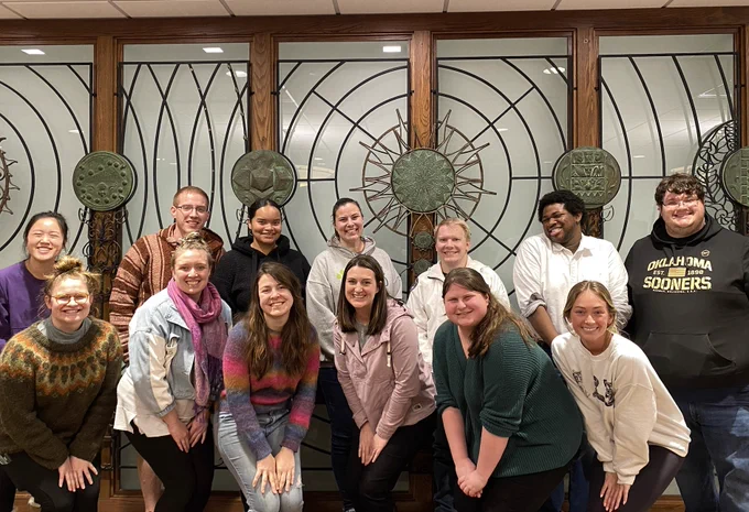 Photo of 13 students in front of History of Science screen at the 5th floor Special Research Collections in Bizzell Memorial Library (all with great smiles!)