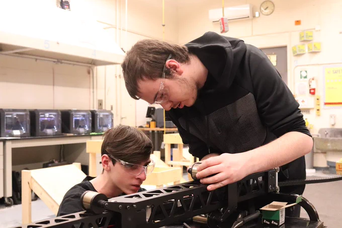 Two students working on the arm for a robot.