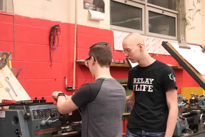 A mentor and a student working on the lathe.