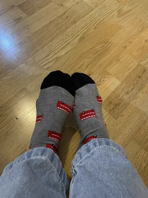 The bottom of jeans with feet covered in grey socks with red double-deckers buses on then.