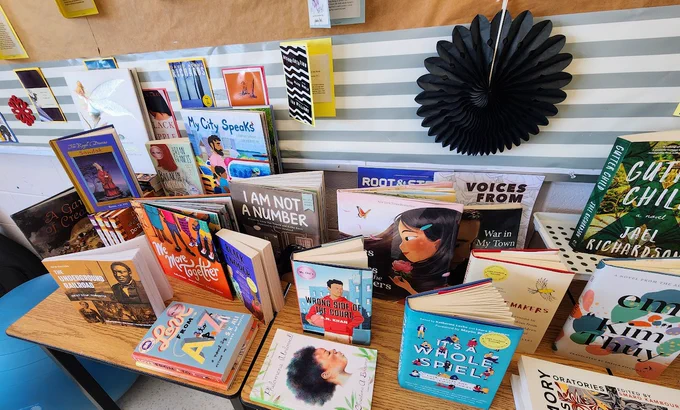 An assortment of books that include novels, creative nonfiction, magazines, and children's picture books, all set on a table in a classroom.