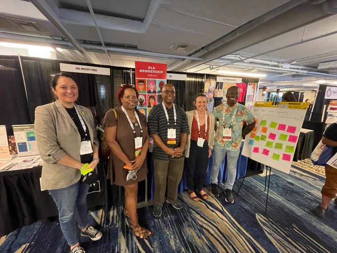 Picture of ALA President Lessa Kanani'opua Pelayo-Lozada and several Libraries Build Business cohort library reps standing in front of the ALA booth at JCLC2022