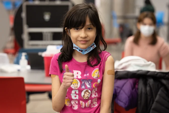Girl wearing a pink shirt gives a thumbs up.