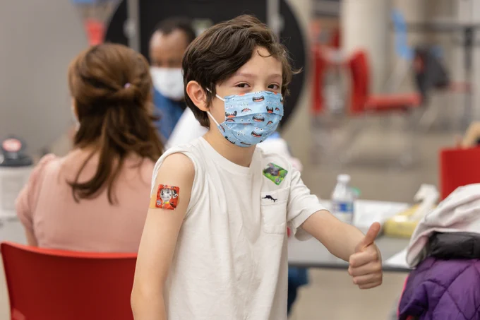 Boy wearing a monster mask and a Paw Patrol bandage on his arm gives a thumbs up.