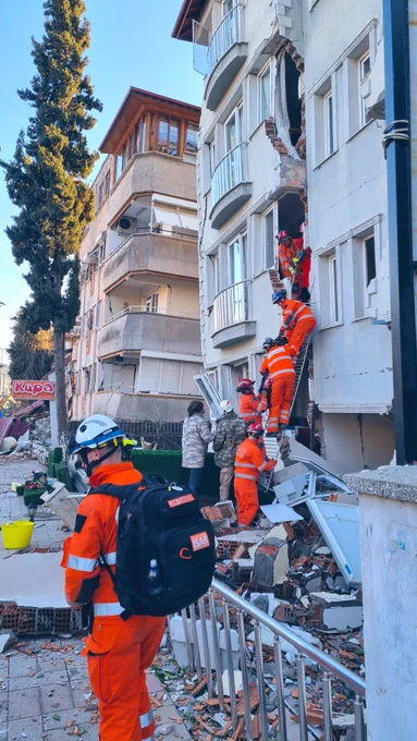 Rescue team passing down a stretcher from a first floor window, surrounded by damaged buildings in Turkey Hatay province