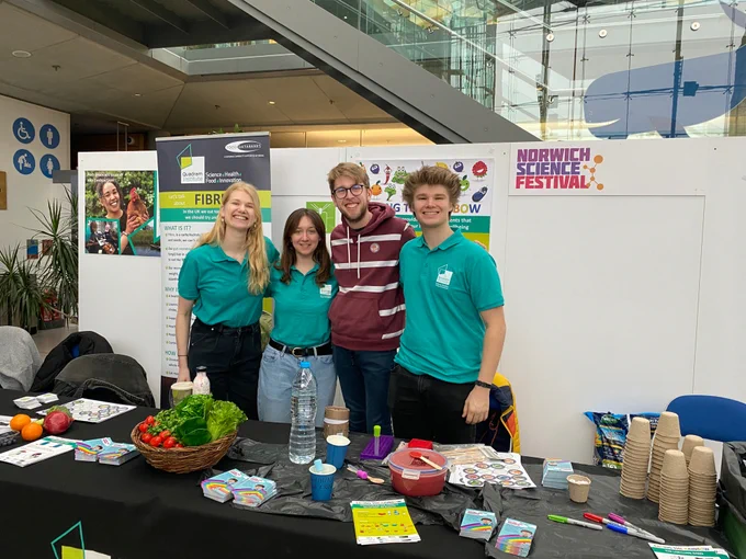 Four young people wearing turquoise polo shirts at a stand at the science festival full of activities based around plant based nutrition 