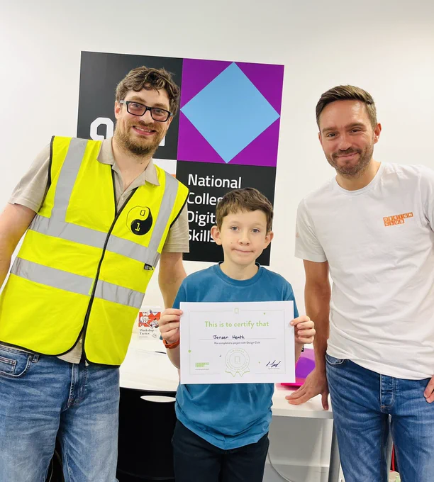 Volunteers James and Lee handing out a certificate to one of our new design club members celebrating a successful project.