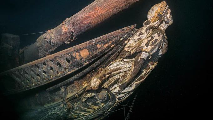 The ornamental figurehead on the bow of a wrecked ship looms out of the darkness at the bottom of the Baltic Sea