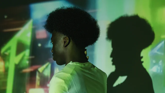 A person stands in green lighting, with their silhouette on the wall behind them