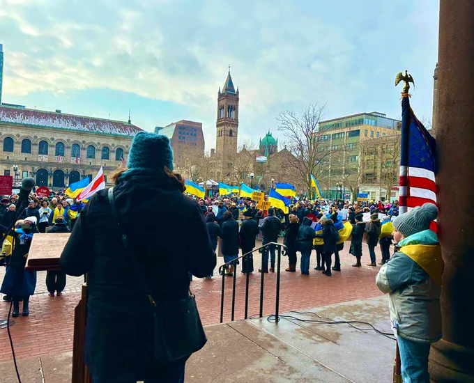 Councilor Kenzie Bok speaks facing a sea of Ukrainian flags and signs in Copley Square, with the American flag to the right.