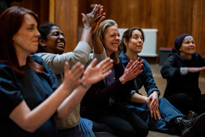 An audience view featuring a group of people clapping and laughing in response to a performance out of view of the camera.