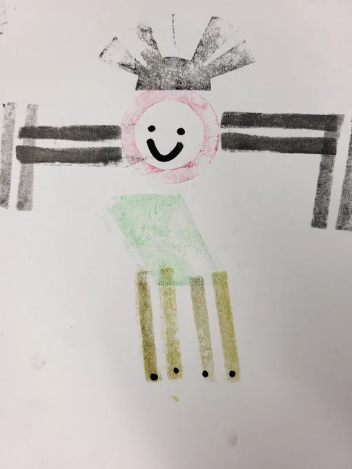 Black, gold, pink and green arrangements of linear shapes have been used to create a robot body. It has a circle body with a smiling face
