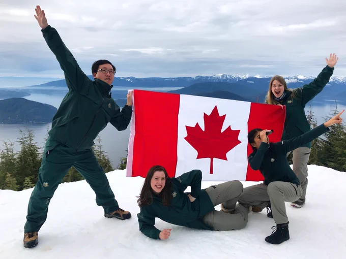 Four Parks Canada employees pose with a Canadian flag in front of Vancouver's mountains.