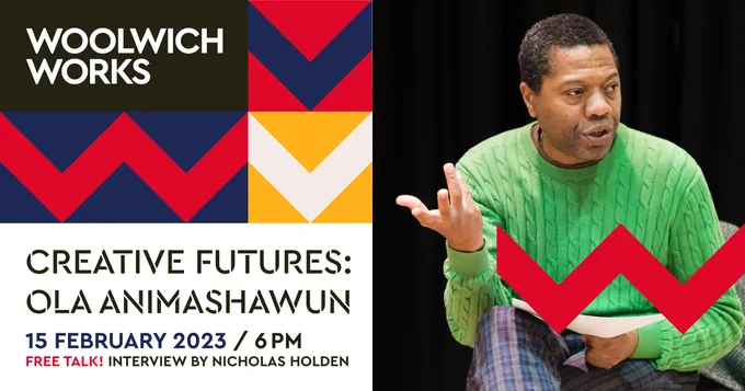 Ola Animashawun seated in a rehearsal room, mid-speaking with papers in hand. He wears a bright green jumper and plaid trousers. Red Woolwich Works chevrons are overlaid in the bottom right of the image.