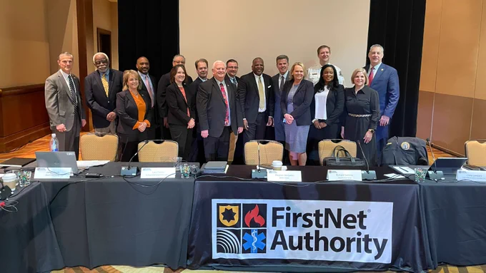 FirstNet Authority Board members stand behind table with FirstNet Authority sign at quarterly Board meeting