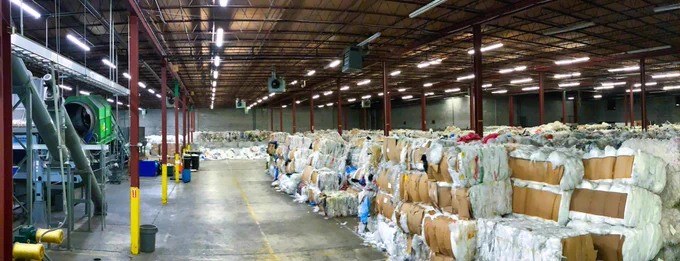 A recycling facility with machinery on the left and bales of plastic material waiting to be recycled on the right. 