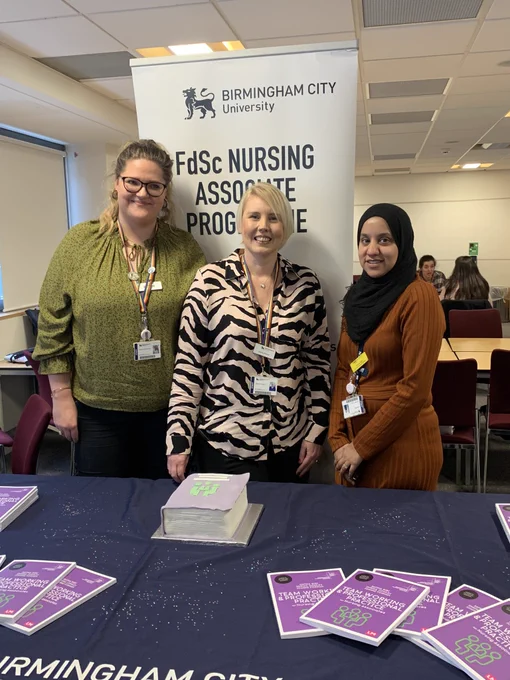 A photo of authors Enrika, Safina & Jo in front of a table containing copies of their book Team working and professional practice for nursing associates