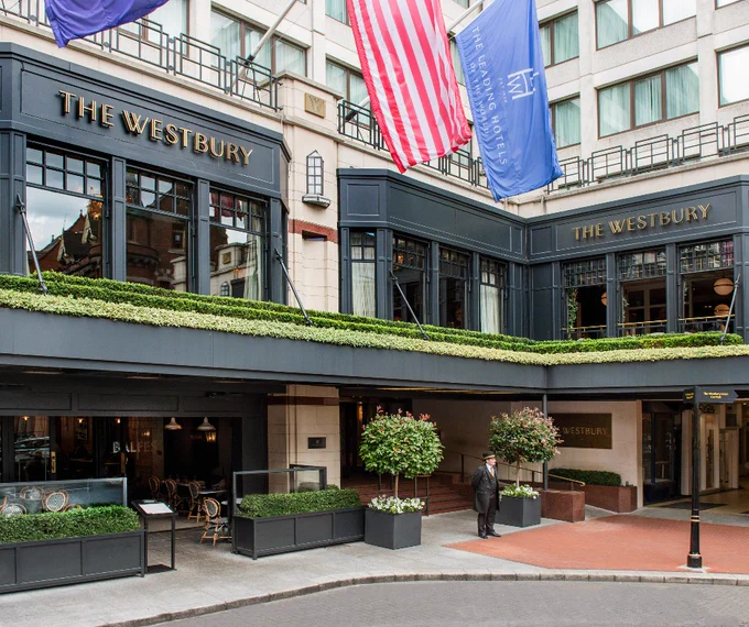 An exterior image of The Westbury, a luxurious 5-star hotel on Dublin's Grafton Street. Outside the hotel you can see the Leading Hotels of the World Flag, as well as a doorman waiting to greet guests.