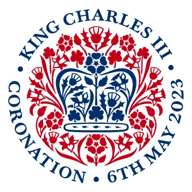 The coronation emblem has a blue crown in the centre with red plants around it and the words King Charles III Coronation 6th May 2023 around the outside.
