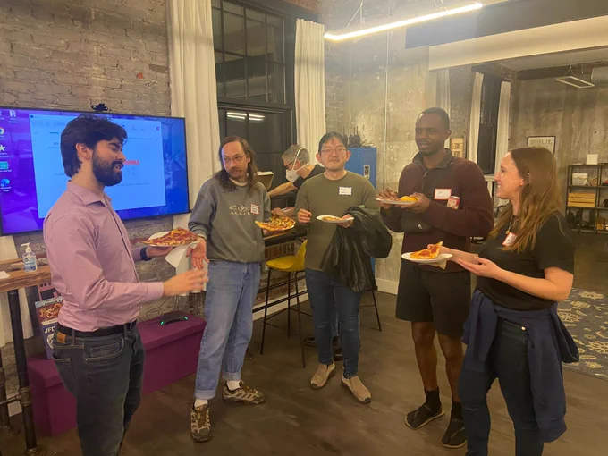 Five civic tech volunteers standing around, smiling and eating pizza