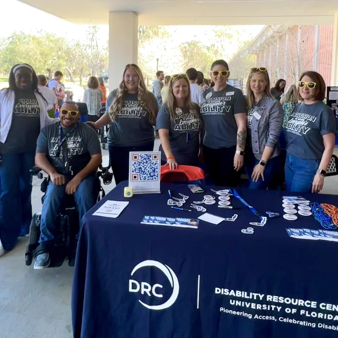 Seven disability resource center staff stand together in their matching “Inclusion is within everyone’s ability” t-shirt behind their table at todays Giving Day event.