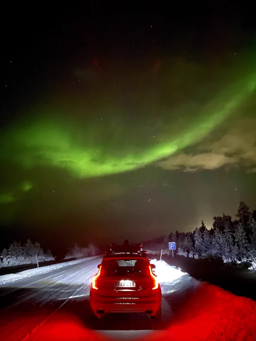 White XC90 Volvo on the side of a snowy road, under Northern Lights.