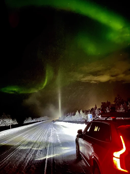 White XC90 Volvo on the side of a snowy road, under Northern Lights.